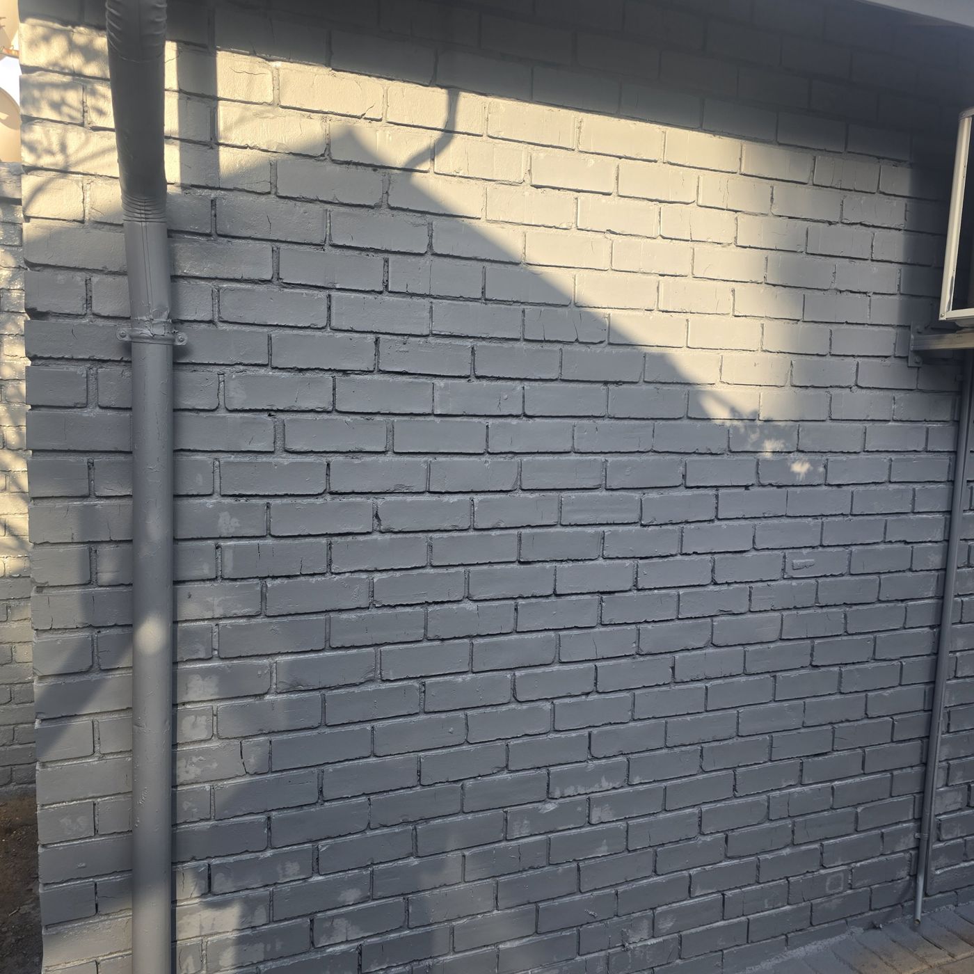 Exterior brick wall painted grey, with the downpipe painted to match
