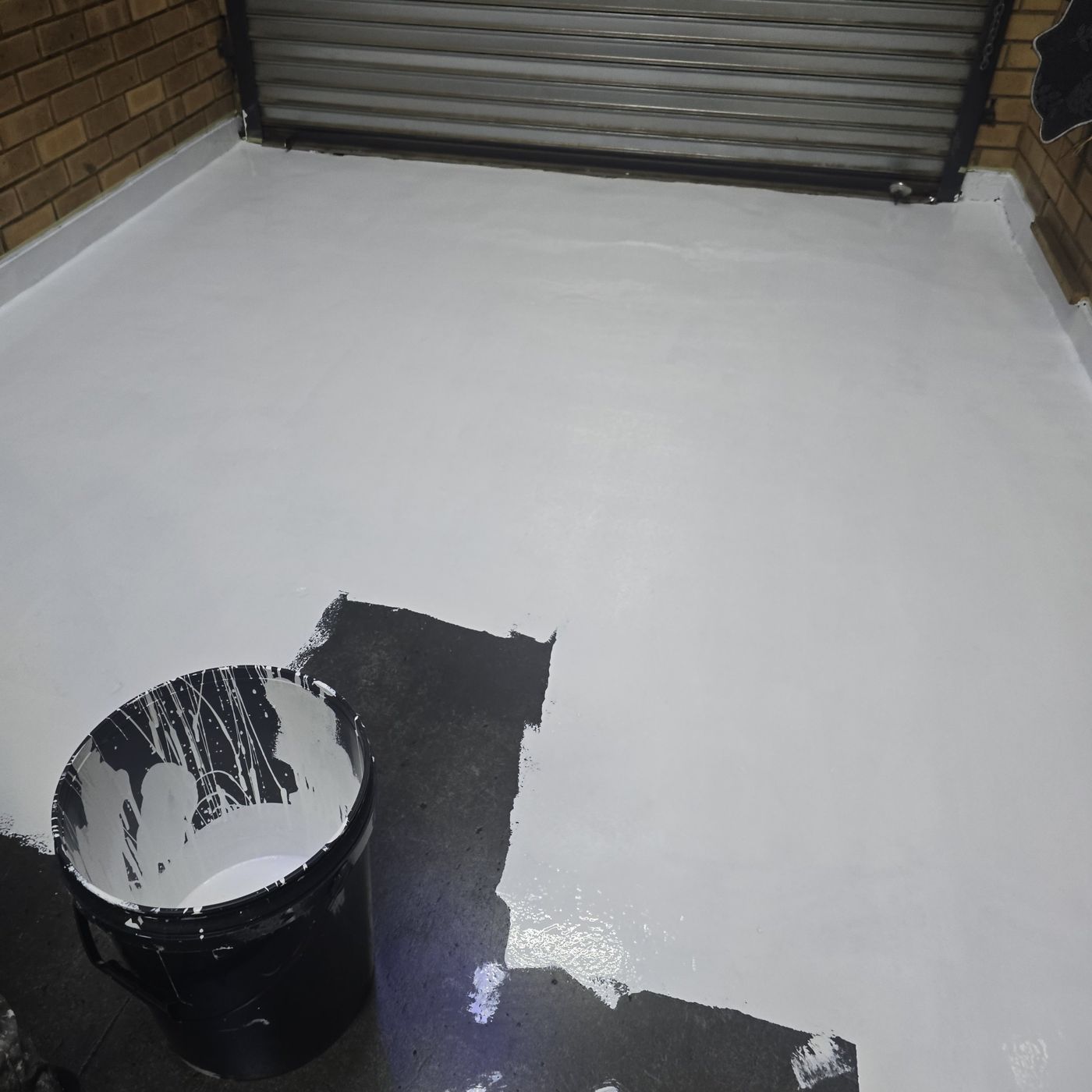 Grey epoxy base coat being rolled onto dark concrete