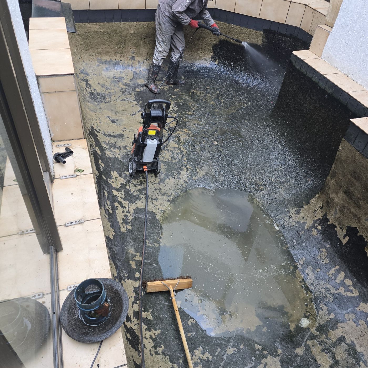 Pond being pressure washed, with the old coating peeling off